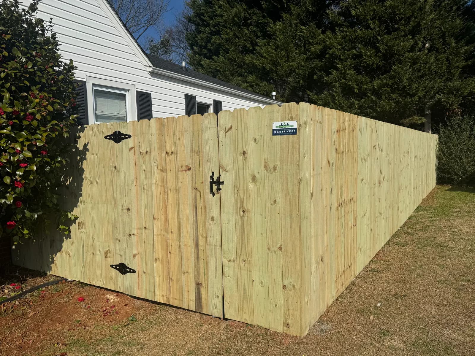 Dog-ear wood privacy fence with a gate and black hardware beside a white house.