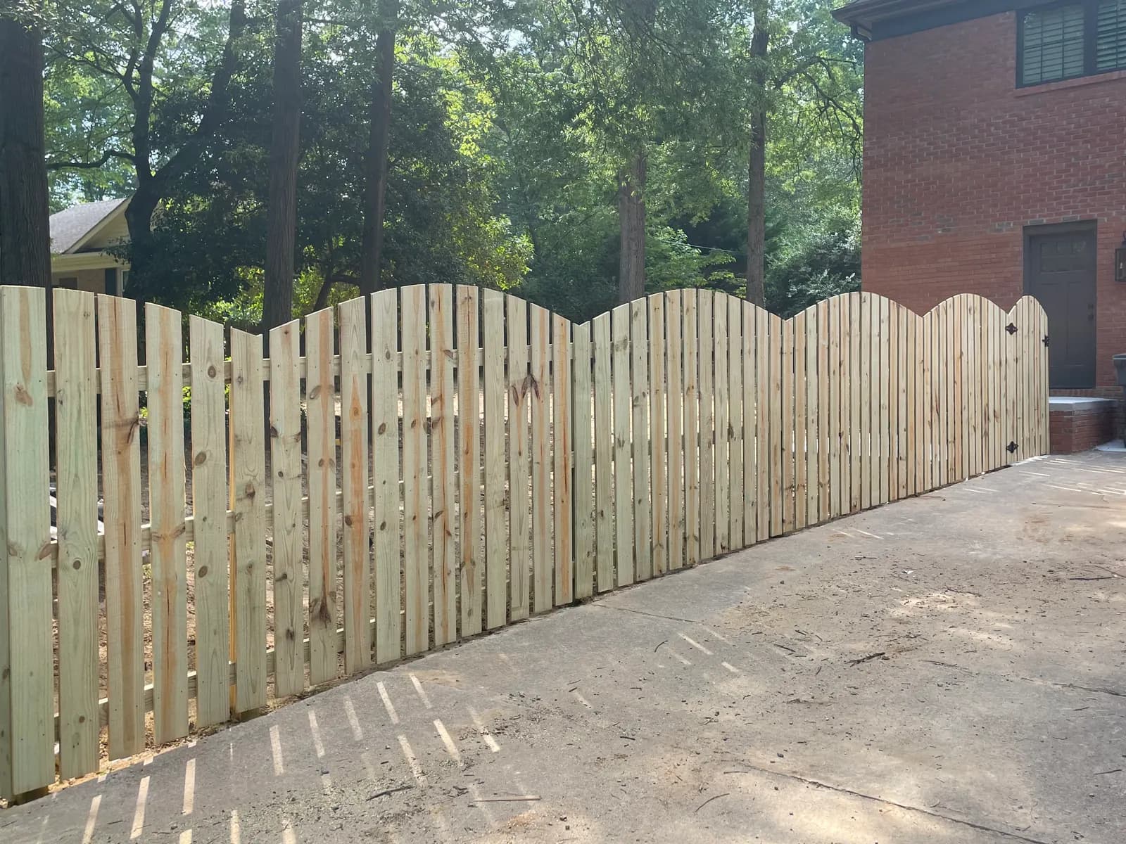 Wood semi-privacy fence with an arched scalloped top along a driveway.