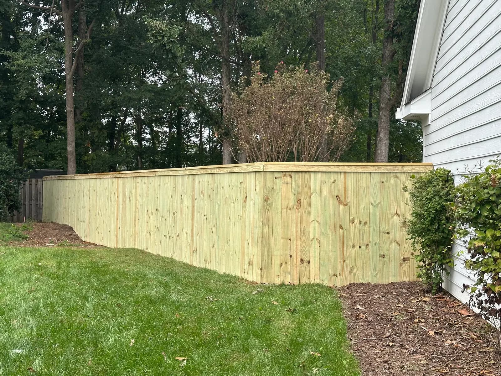 Wood privacy fence with cap and trim beside a white house.