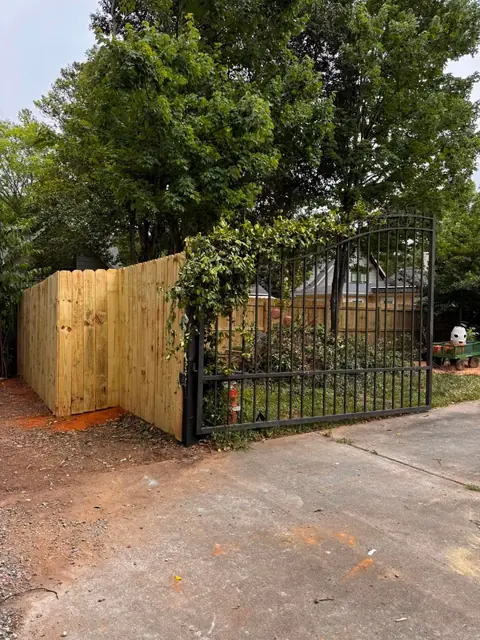 Wood privacy fence with a black arched metal drive gate.