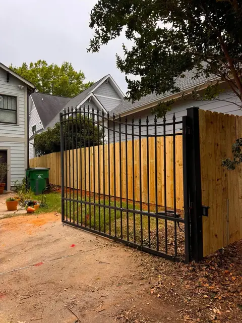 Black arched metal drive gate hung beside a wood privacy fence.
