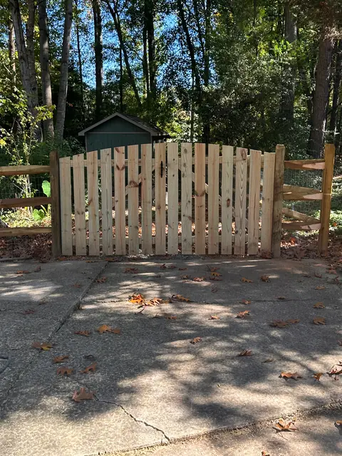Arched wood double drive gate set in a split rail fence at the end of a concrete driveway.