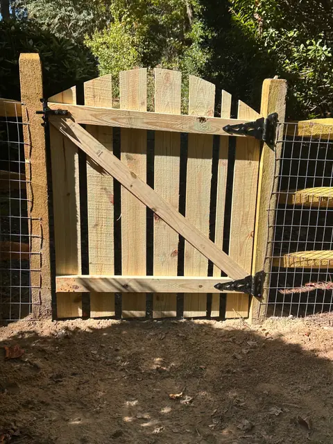 Arched wood gate with black strap hinges set in a split rail fence with welded wire.