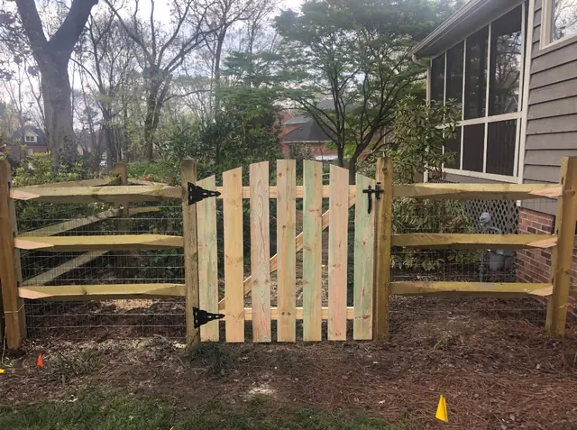Arched wood picket gate in a split rail fence with welded wire.