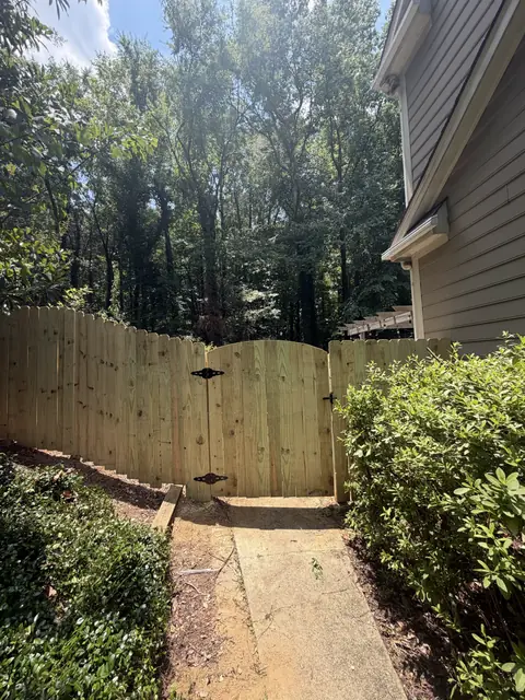 Arched wood privacy gate with black decorative hinges at the end of a path.