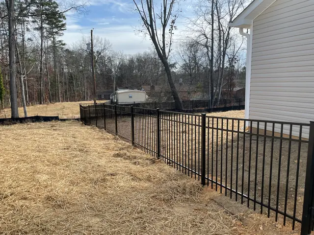 Black aluminum fence with a flat top rail running along the side yard of a house with white siding.