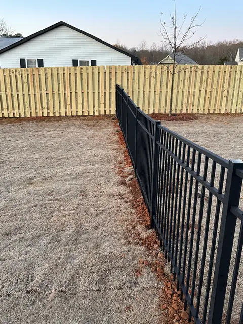 Black aluminum fence meeting a wood fence at a rear property line.