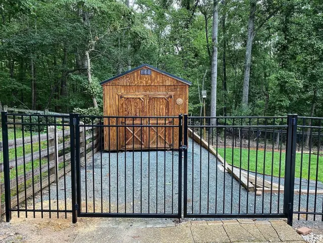 Black aluminum fence with a double gate opening onto a gravel pad with a wood shed.
