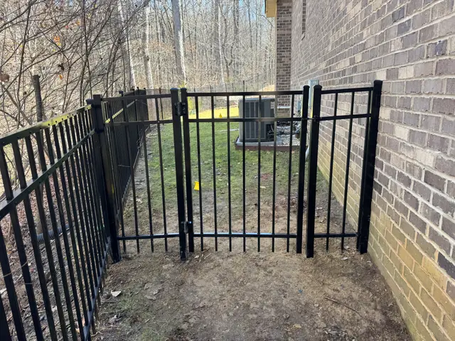 Black aluminum double gate in a side yard next to a brick house.