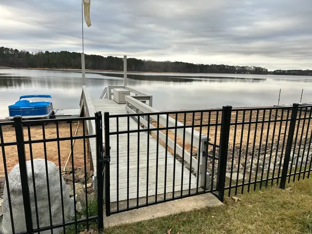 Black aluminum fence and gate at the entrance to a boat dock on a lake.