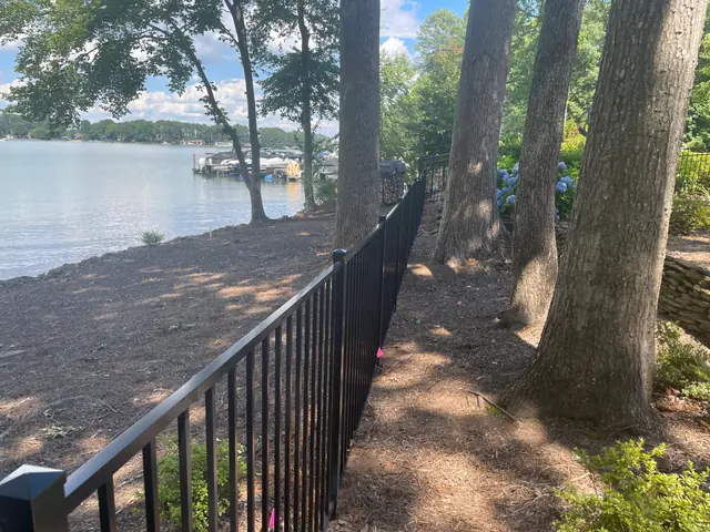 Black aluminum fence running between trees along a lake shoreline.