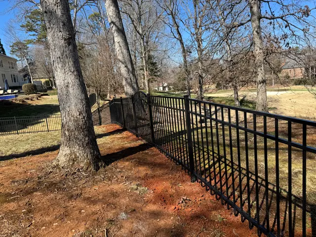 Black aluminum fence following a slope between mature trees.