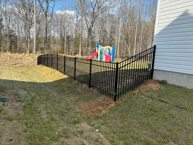 Black aluminum fence racked down a slope beside a house, with a play set in the yard.