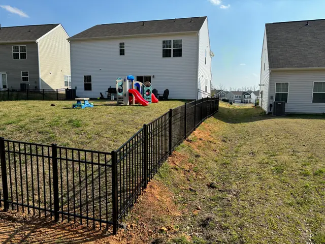 Black aluminum fence following a graded slope behind two-story homes.