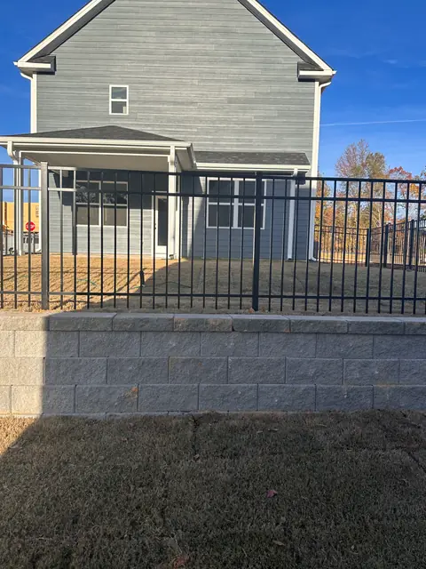 Black aluminum fence installed along the top of a block retaining wall behind a two-story house.