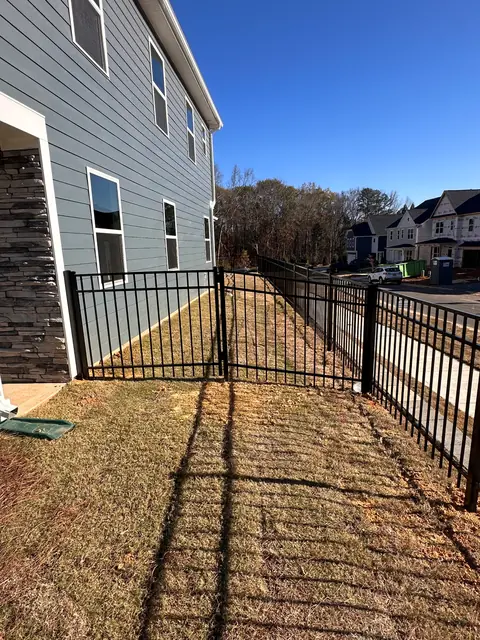 Black aluminum fence with a walk gate along the side of a gray two-story house.