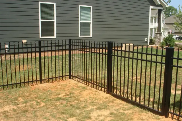 Black aluminum fence with a walk gate in front of a dark gray house.