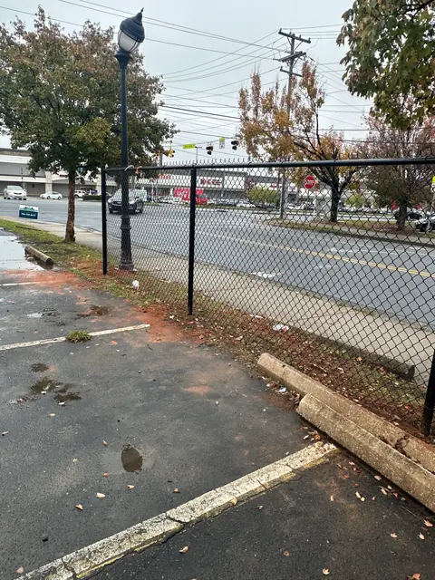 Black vinyl coated chain link fence along a parking lot.