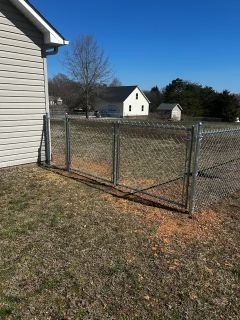 Galvanized chain link double gate beside a house.