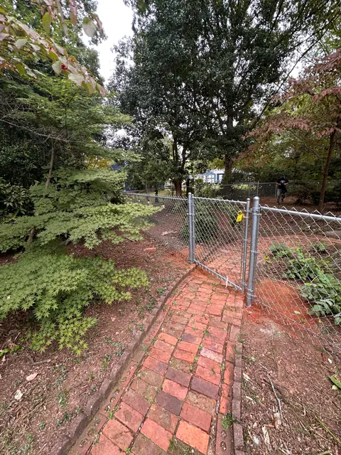 Galvanized chain link gate at the end of a brick garden path.