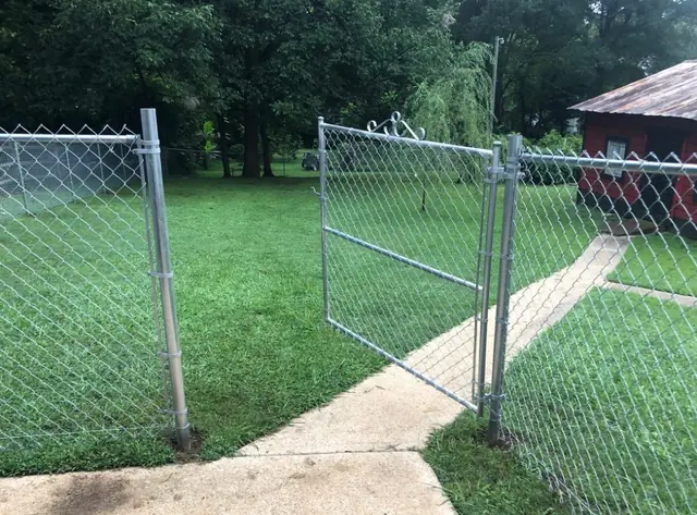 Galvanized chain link walk gate standing open over a concrete path.