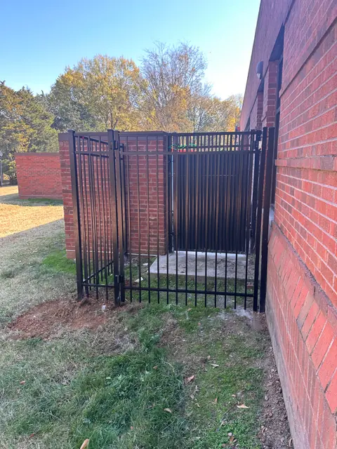 Black aluminum fence and gate enclosing an area beside a brick commercial building.