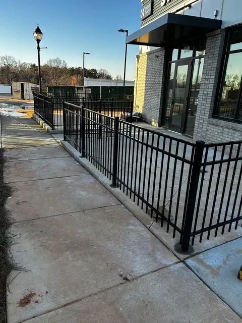 Black aluminum fence around a patio at a commercial storefront.