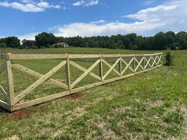 Wood crossbuck fence with wire mesh running across an open pasture.