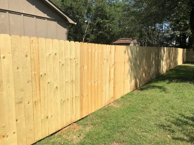 Long run of dog-ear wood privacy fence along a lawn.