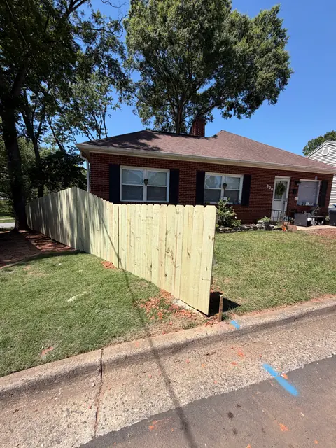 Dog-ear wood privacy fence along the street side of a brick house.