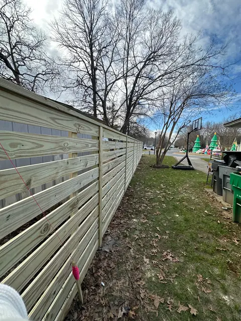 Horizontal board wood fence with spaced boards along a side yard.