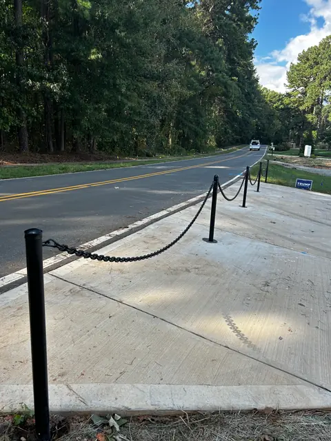 Black post and chain barrier along the edge of a concrete driveway apron.