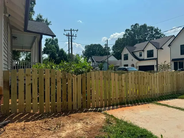 Wood fence with spaced boards and a scalloped top along a front yard.