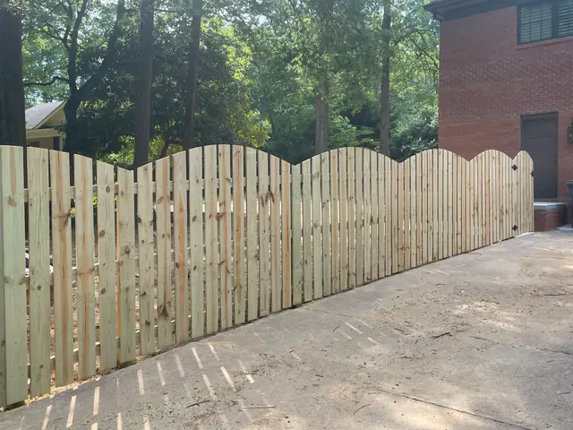 Wood semi-privacy fence with an arched scalloped top along a driveway.