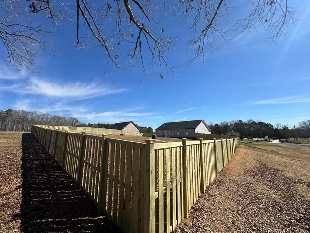 Shadowbox wood fence with post caps running along an open field.