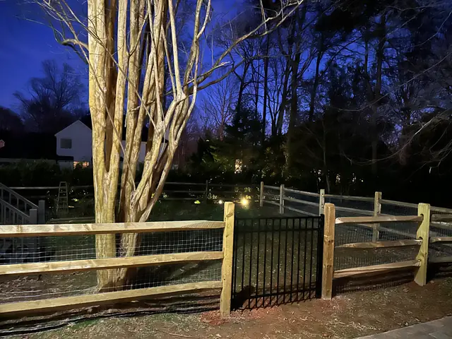 Split rail fence with welded wire and a black metal gate, photographed at dusk.