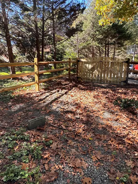 Three-rail split rail fence with welded wire and a wood gate in a wooded yard.