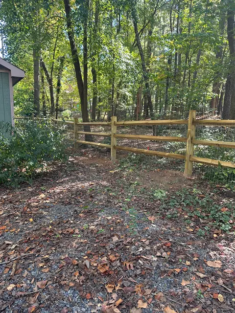 Three-rail split rail fence crossing a wooded lot.