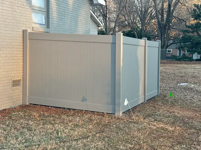 Tan vinyl privacy fence enclosure beside a brick house.