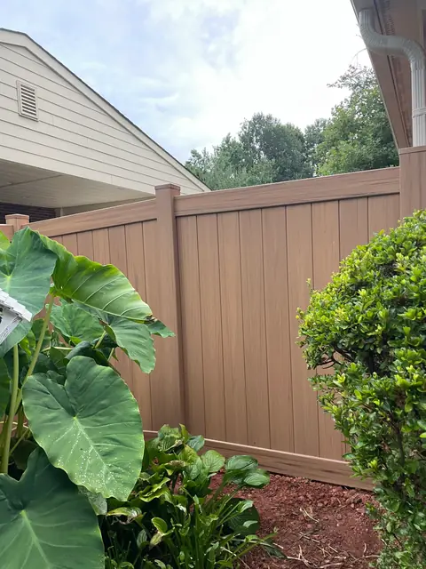 Tan vinyl privacy fence behind garden plants.
