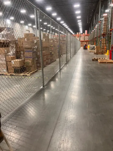 Tall chain link partition running the length of a warehouse aisle.