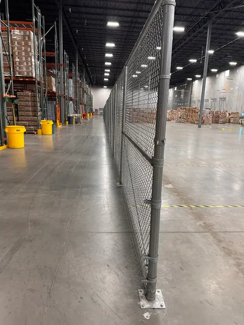 Tall chain link partition with floor-mounted steel posts in a warehouse.