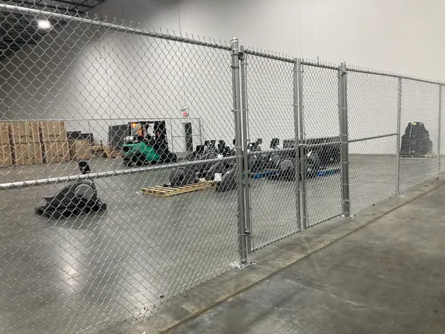 Galvanized chain link fence with a double swing gate inside a warehouse.