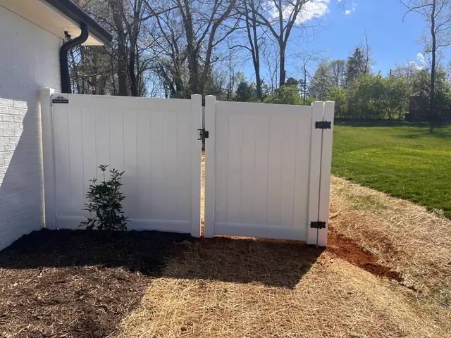 White vinyl privacy double gate beside a white brick house.