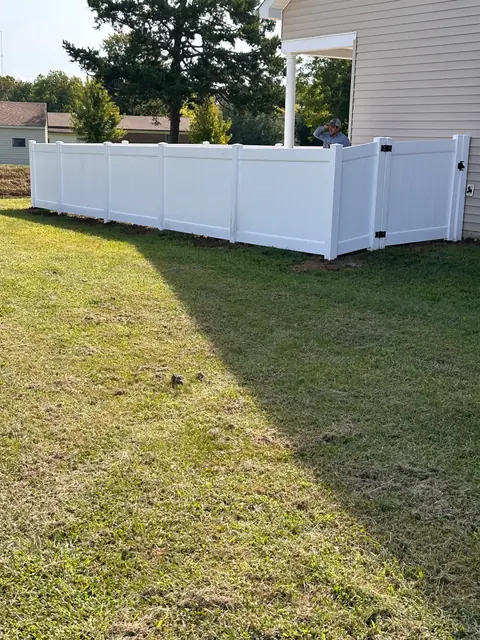 White vinyl privacy fence with a gate enclosing a small yard beside a house.