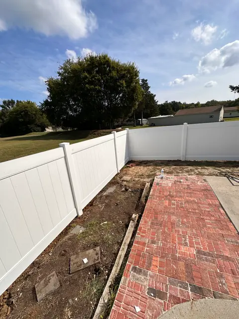 White vinyl privacy fence around a patio with a brick walkway.
