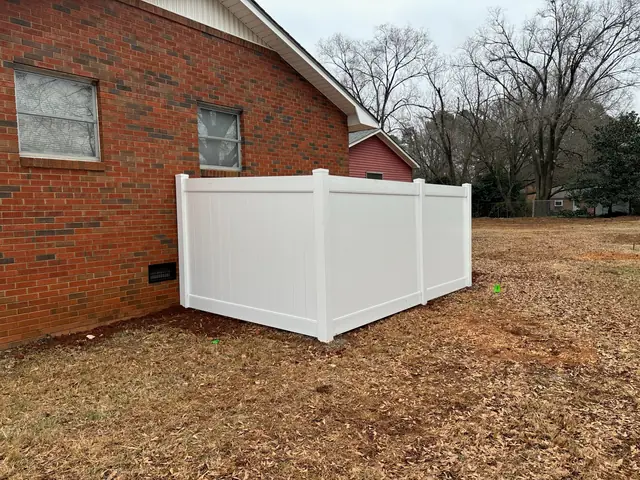 White vinyl privacy fence enclosure at the corner of a brick house.