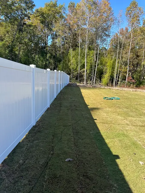 Long run of white vinyl privacy fence beside a lawn.