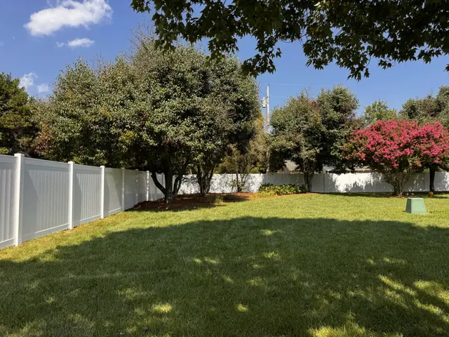 White vinyl privacy fence behind crepe myrtle trees.