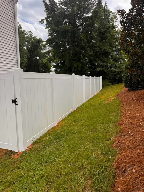 White vinyl privacy fence with a gate along a side yard.